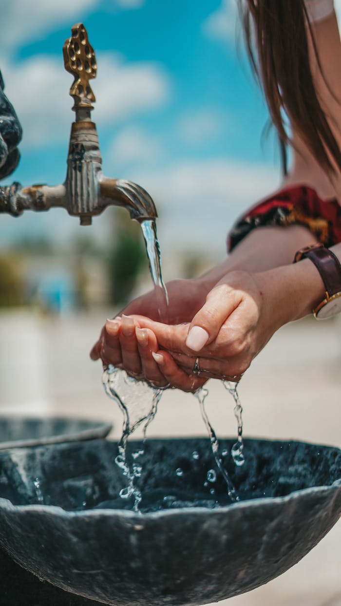 Refreshing scene of a woman washing hands at an outdoor tap on a sunny day.