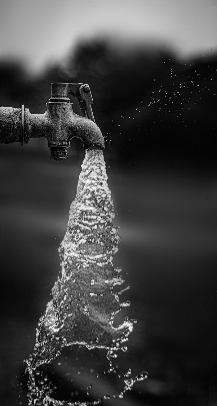 A striking black and white image capturing flowing water from a rustic outdoor faucet.