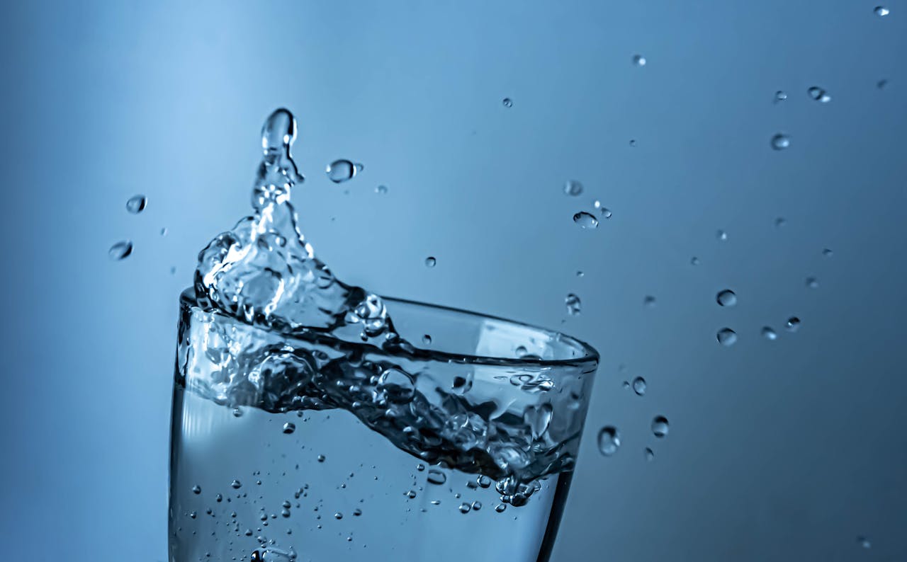 A dynamic splash of water in a clear glass against a blue background.